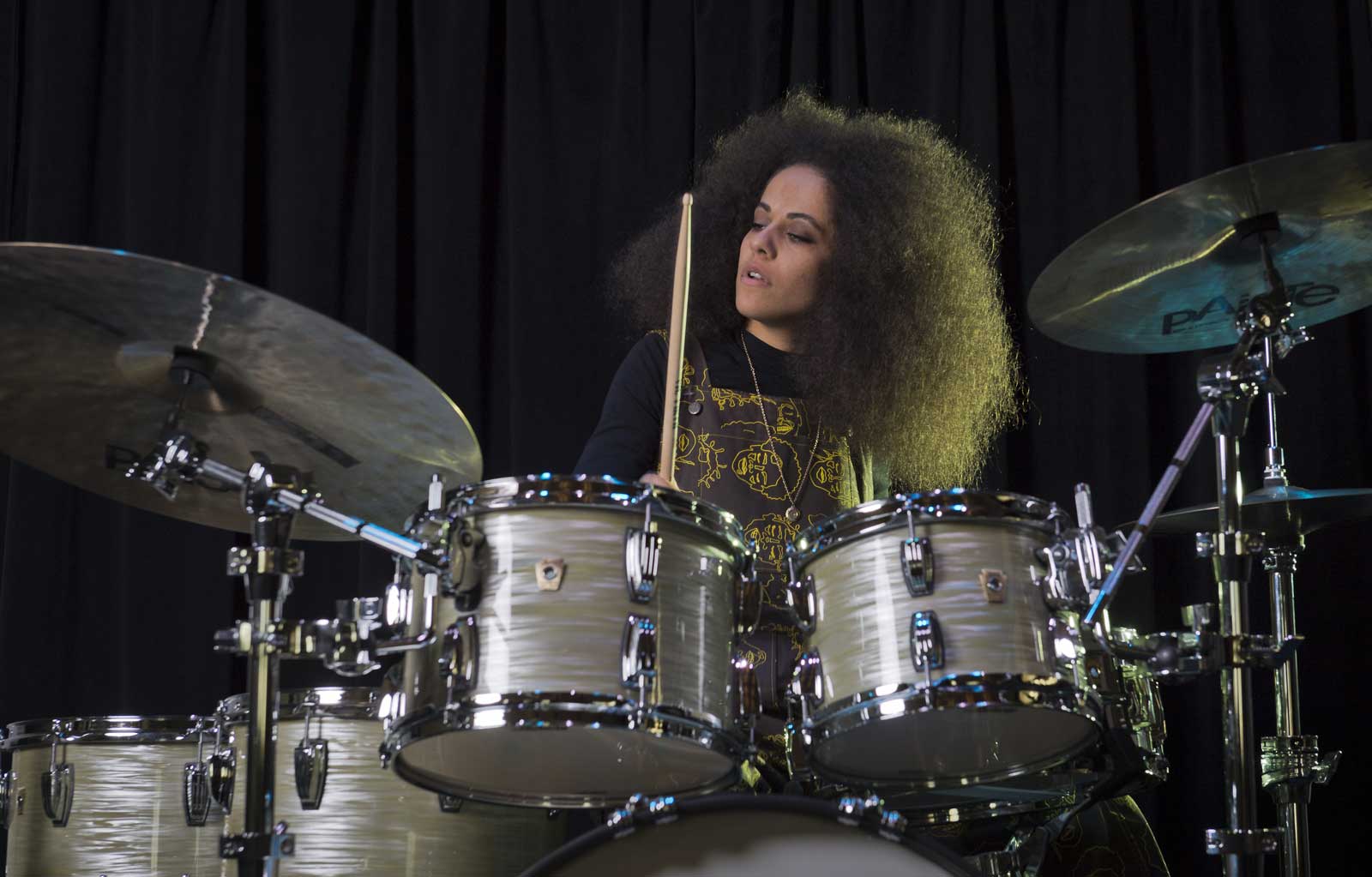 Drummer Jas Kayser is sitting behind a drum set against a black backdrop