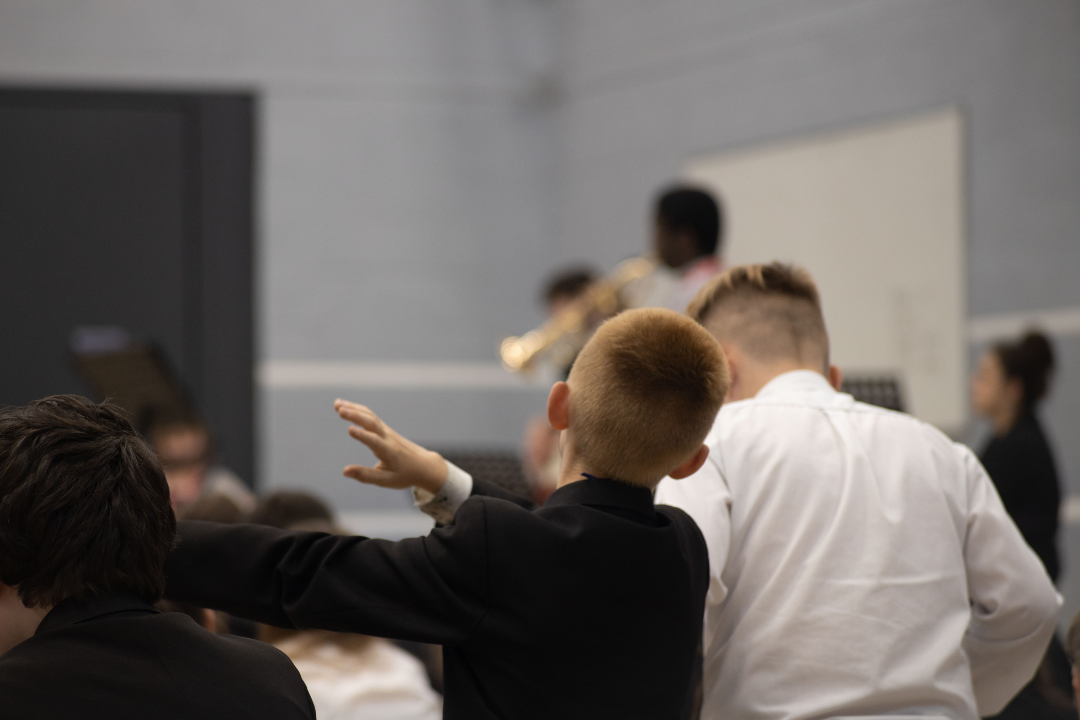 Two young boys in a school watching a quintet of musicians perform. The young people are waving their hands in the air.