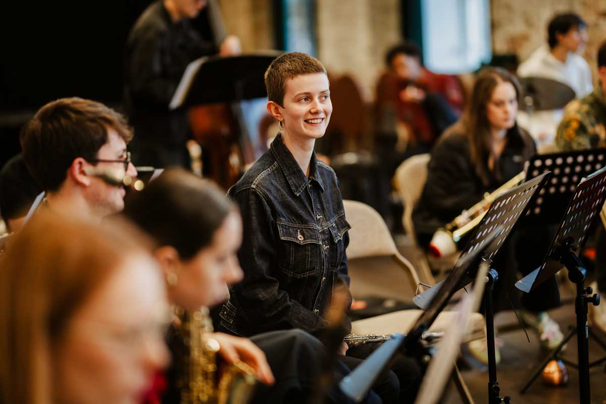 A member of the orchestra is smiling amongst the other players who are blurry