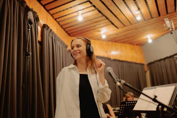 Musical Director Olivia Murphy looks to the left of the camera smiling. She is wearing headphones in the process of a studio recording