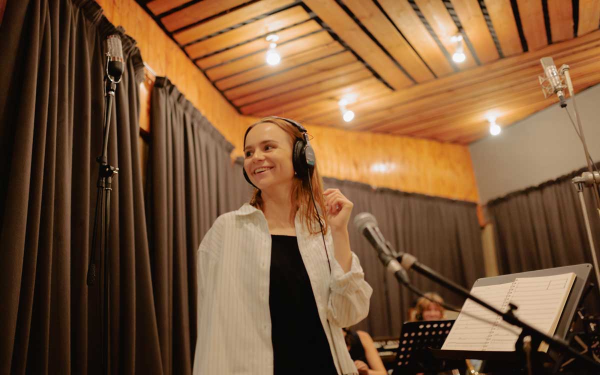 Musical Director Olivia Murphy looks to the left of the camera smiling. She is wearing headphones in the process of a studio recording 