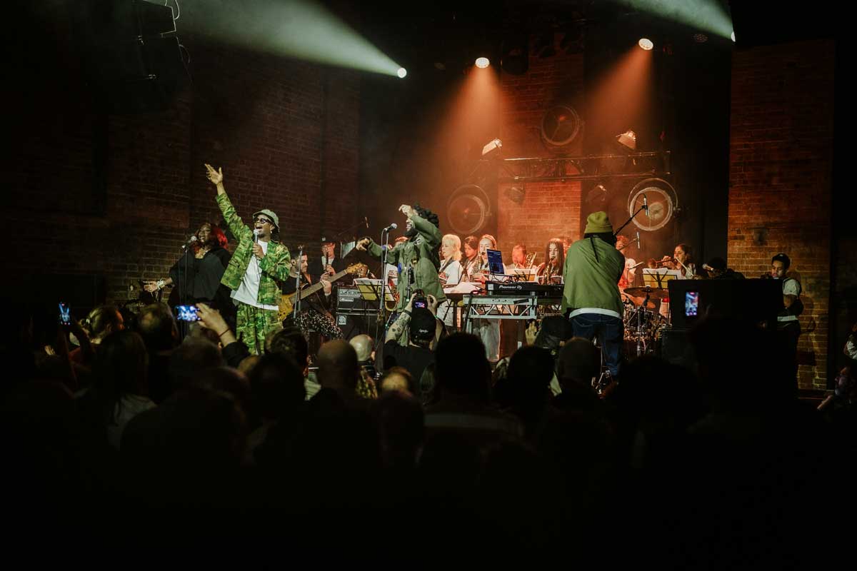 1-Steam-Down-&-NYJO-1C6A5525_WEB A gig is taking place, steam down stands front of stage dressed in khaki, engaging with the crowd, arms in the air